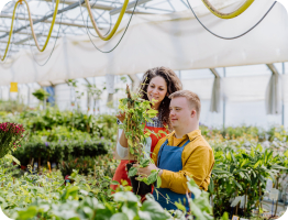 A woman smiling at a younger man. They are in a large garden centre and both wearing aprons.