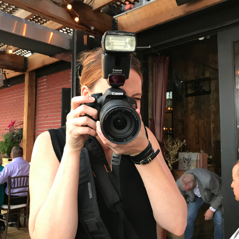 A Lady with brown hair holds a camera up to her face to take a picture.