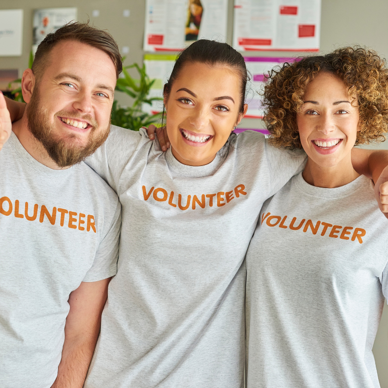 3 people in grey shirts with volunteer pose arm in arm, smiling for the camera