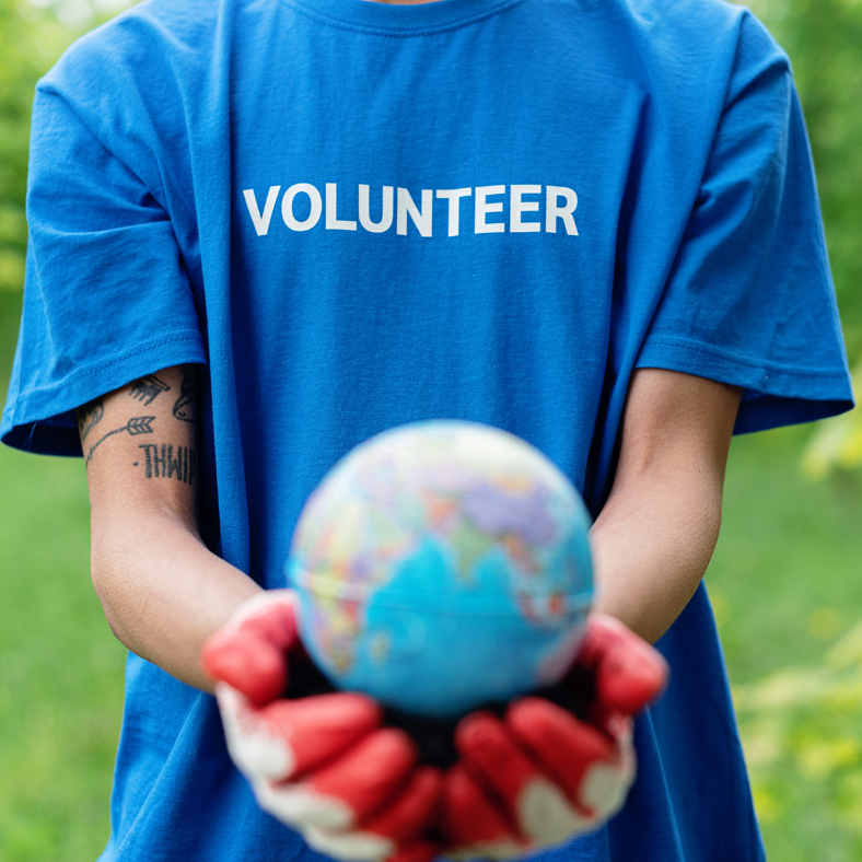 the torso of a person wearing a blue shirt with Volunteer on it, holding a small globe in their gloved hands.