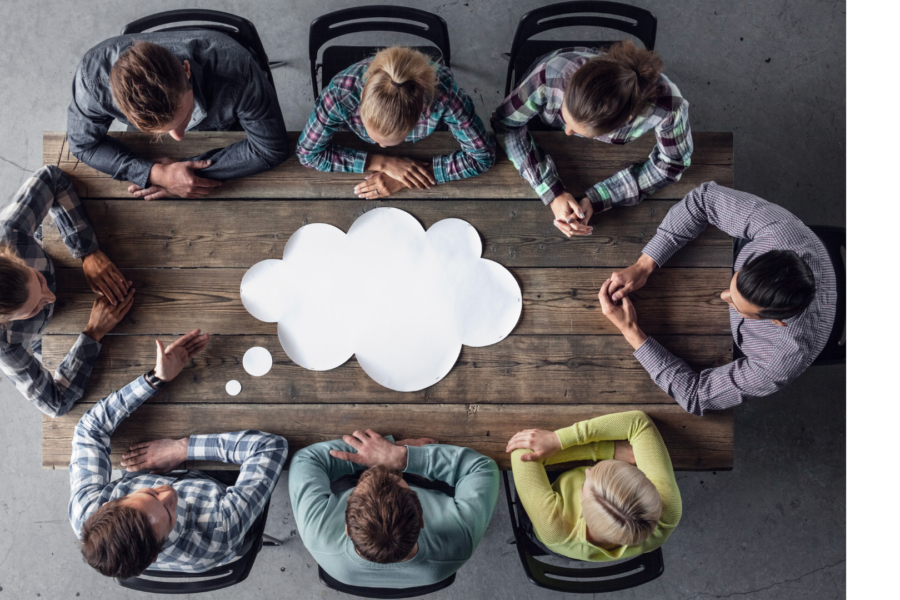 7 people sitting around a large wood desk. There is a large white thinking cloud on the desk