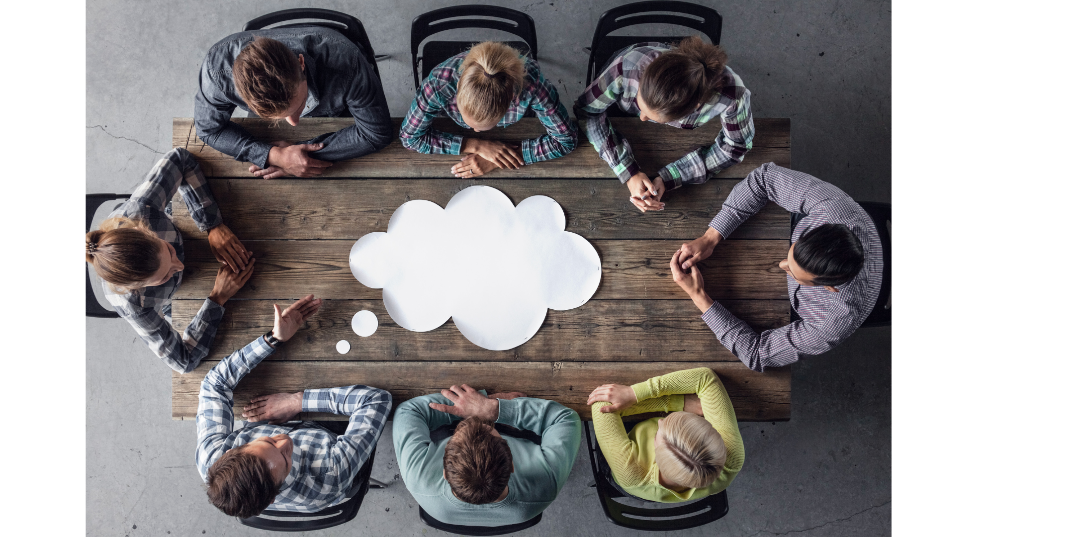 7 people sitting around a large wood desk. There is a large white thinking cloud on the desk