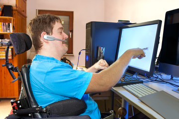 Man working at the computer with headset. He is sitting in an electric wheelchair