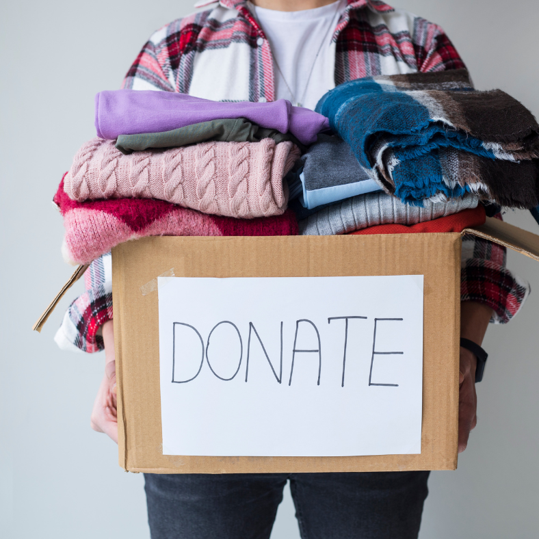 A person holds a cardboard box of clothes and blankets with donate written on the front