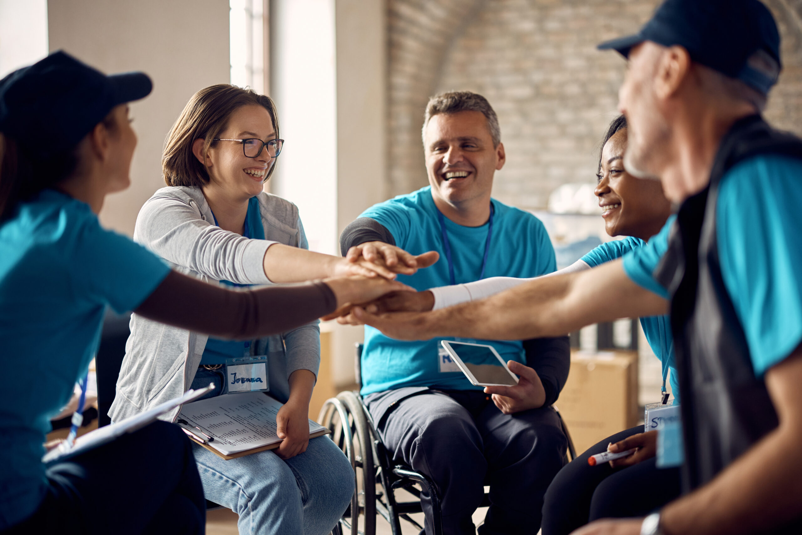 5 people all wearing bright blue tshirts sitting in a circle with their hands together in the middle.