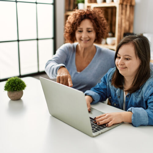 An older woman pointing to an open laptop. A younger woman is using the computer