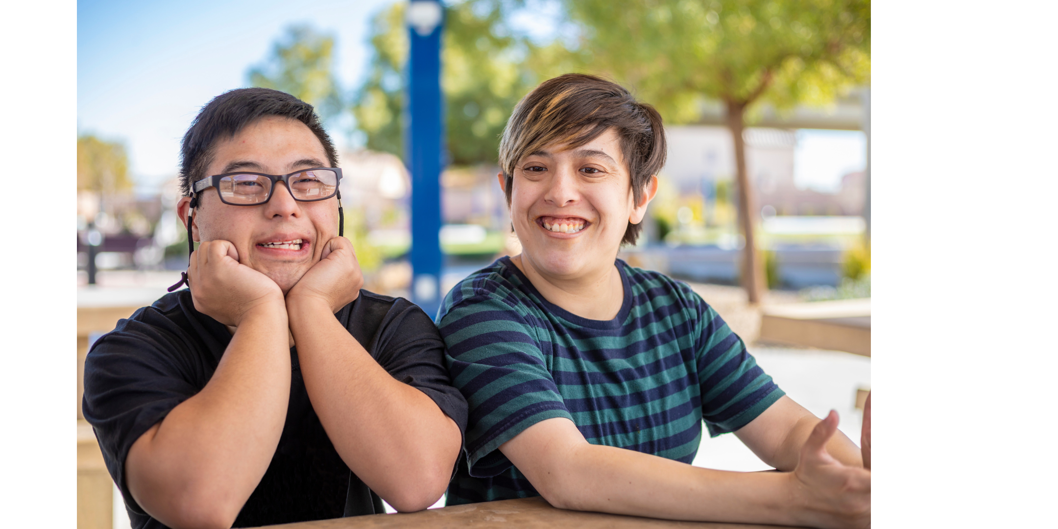 Two young people smiling and sitting on a bench in a park