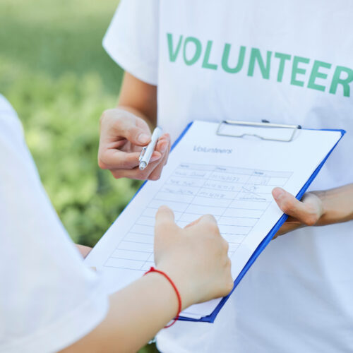 volunteer sign up clipboard held by one volunteer offering the pen to another volunteer
