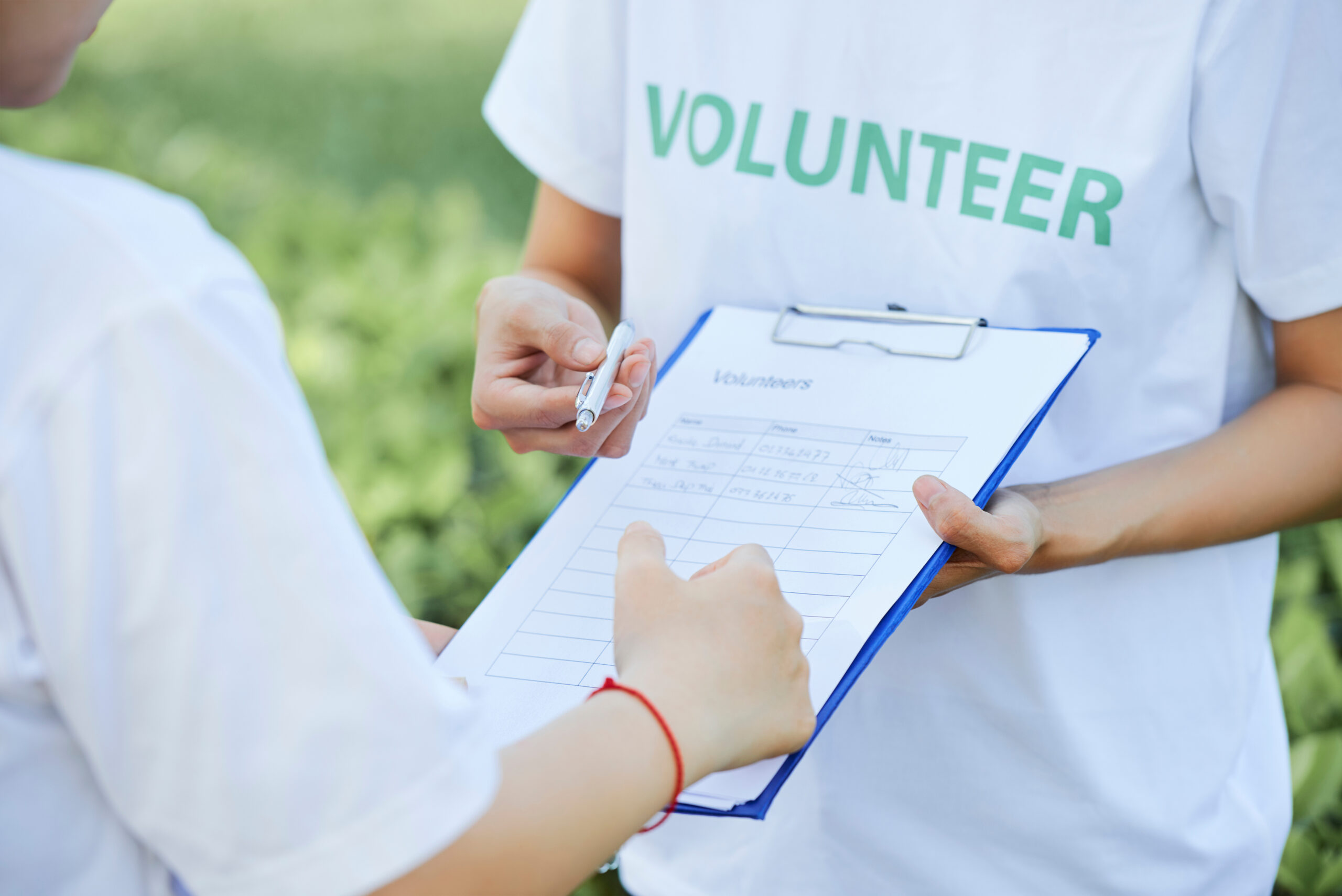 volunteer sign up clipboard held by one volunteer offering the pen to another volunteer
